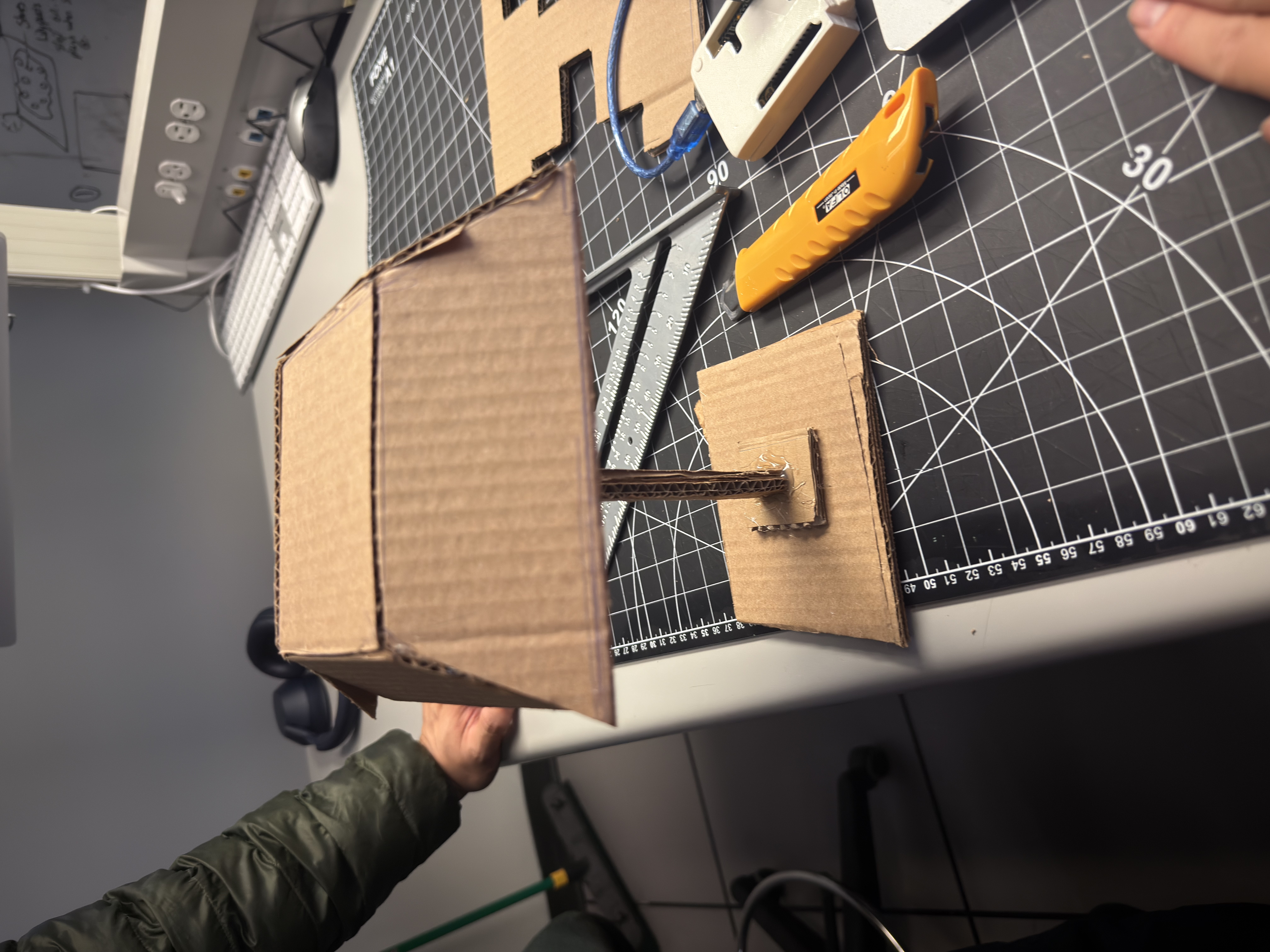 Step 4 — Joinery & cable planning: top view to inspect glue points and cardboard grain; leave channels and tie points for future light/sensor wiring. Hot-glue tacks + tape bridges keep it mod-friendly for revisions.